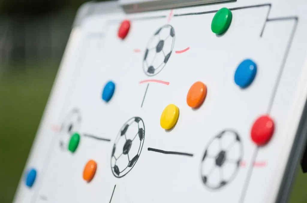 A close-up shot of a soccer tactical whiteboard with colorful magnet markers and strategy drawings, shallow depth of field